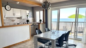 Una cocina moderna con armarios blancos, un comedor con mesa y sillas, y vista al mar a través de amplias ventanas.