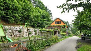 Une maison avec un mur en pierre et une terrasse en bois, entourée d’une végétation luxuriante.