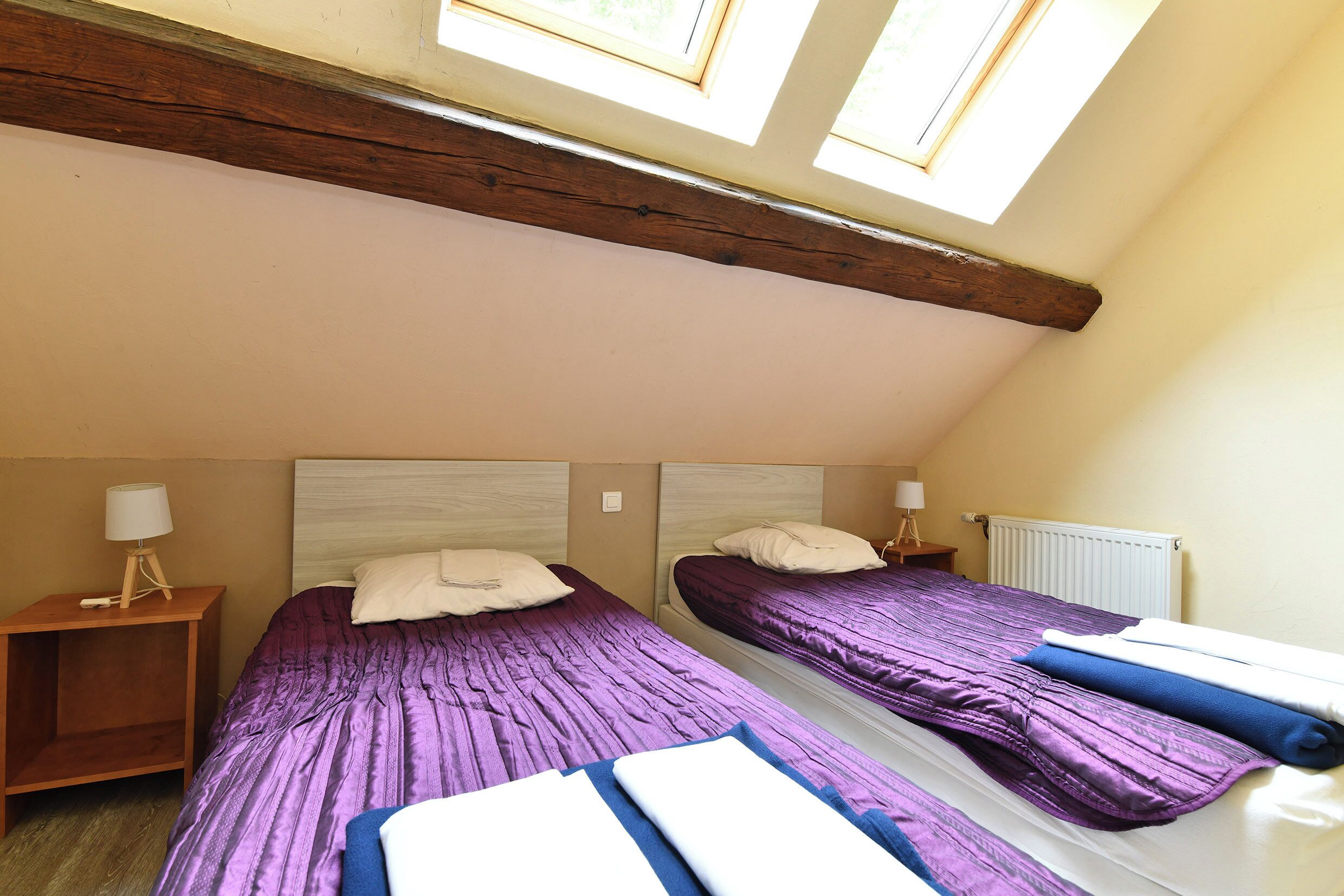 Une chambre avec deux lits, des poutres en bois au plafond et une fenêtre.