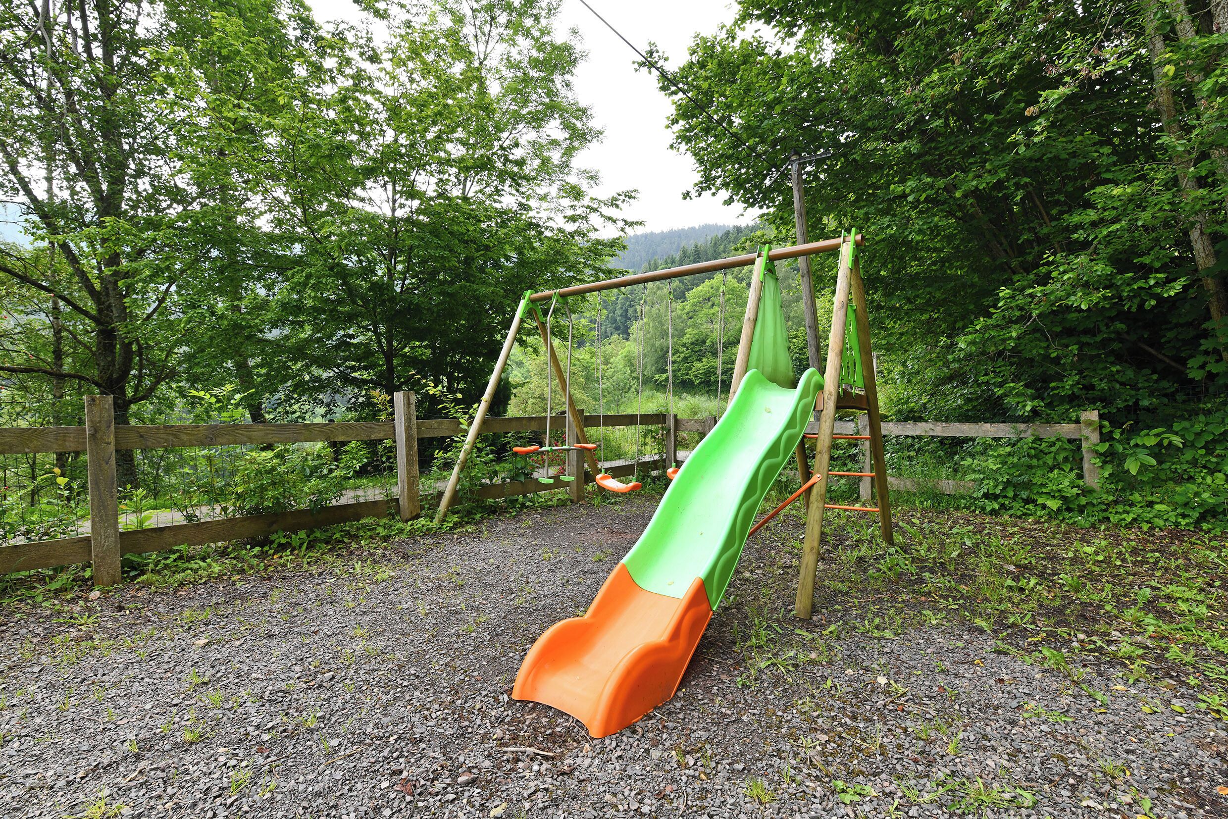 Ein Spielplatz mit Rutsche und Schaukeln inmitten eines bewaldeten Bereichs.