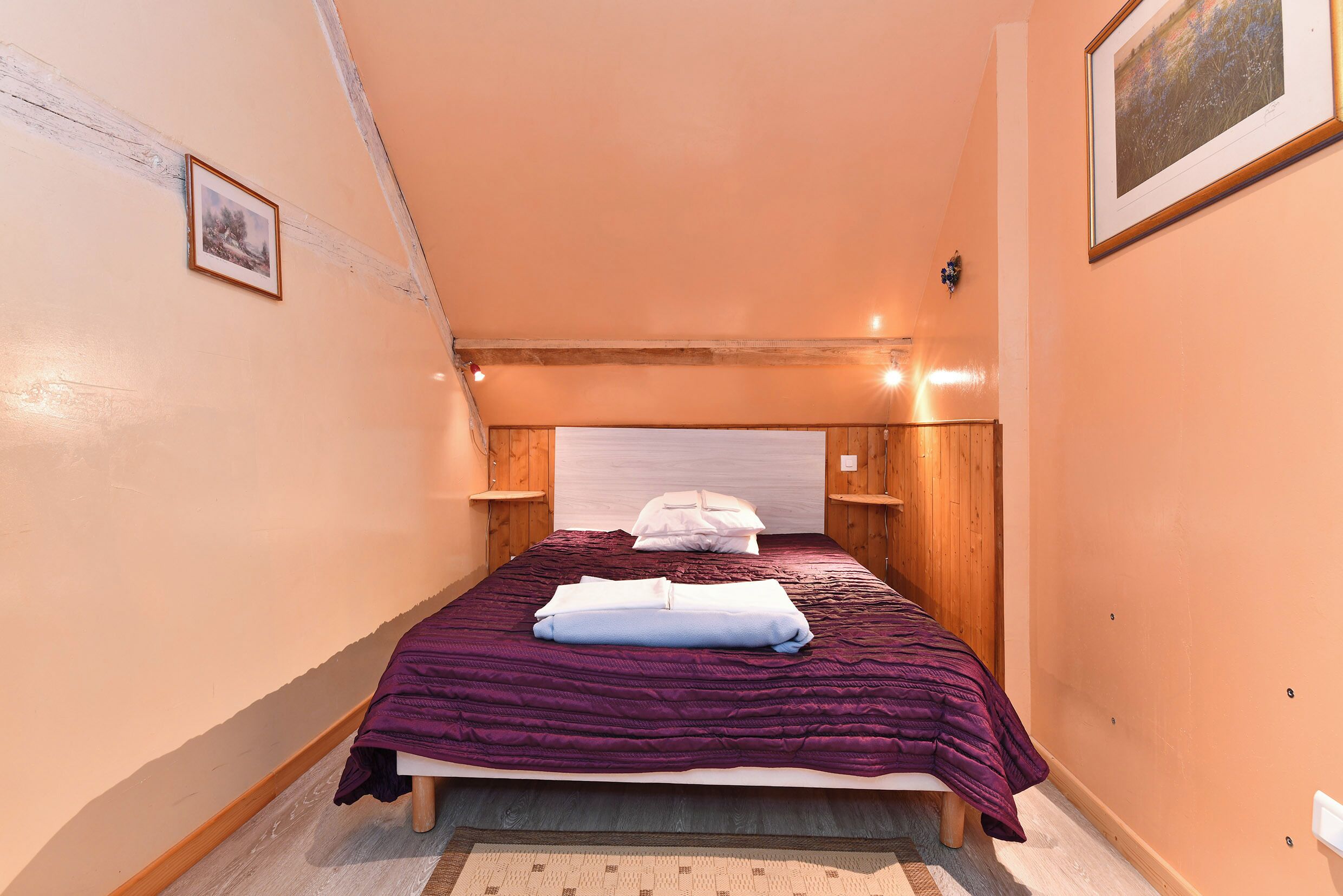 Een smalle kamer met een bed, een houten hoofdbord en een enkel lijstwerk met een afbeelding aan de muur.