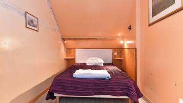 Een smalle kamer met een bed, een houten hoofdbord en een enkel lijstwerk met een afbeelding aan de muur.