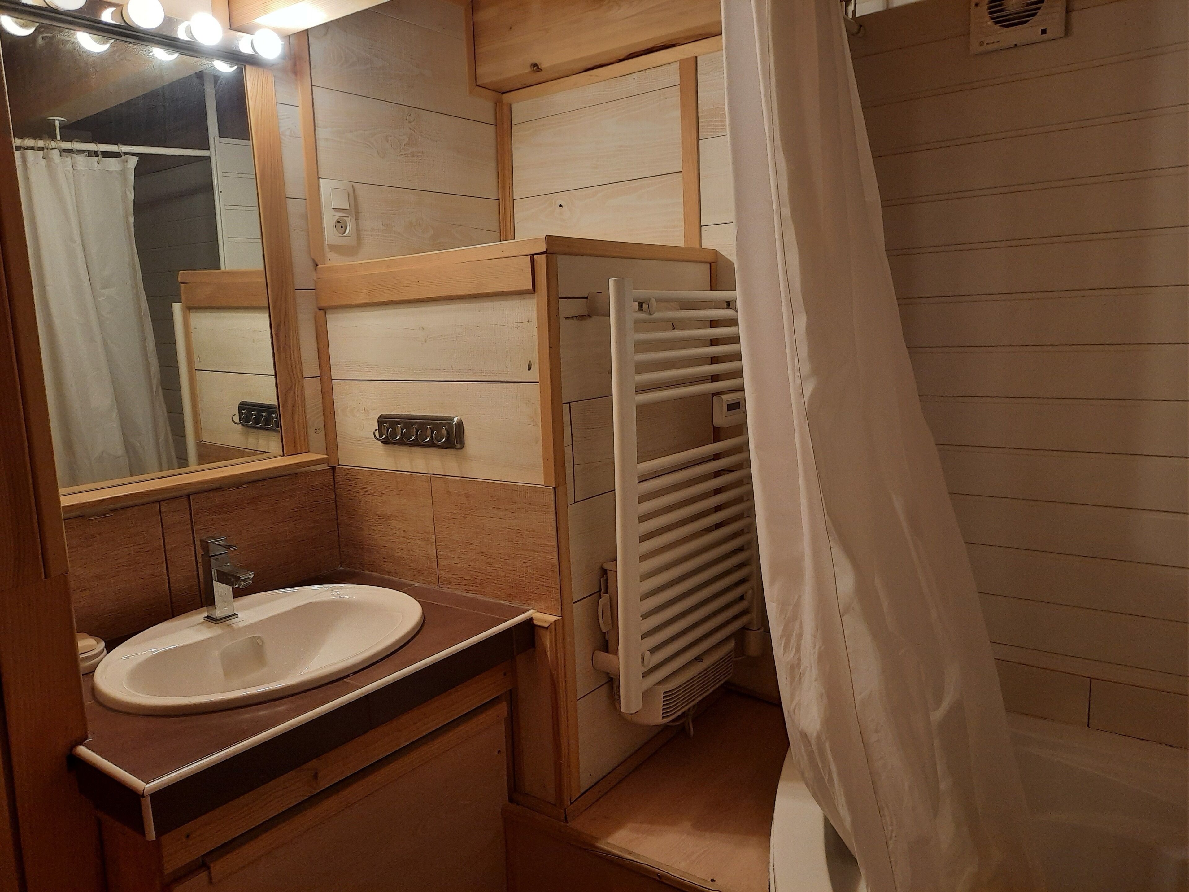 A bathroom with a wooden vanity, a sink, a mirror with lights, a towel rack, and a shower curtain.