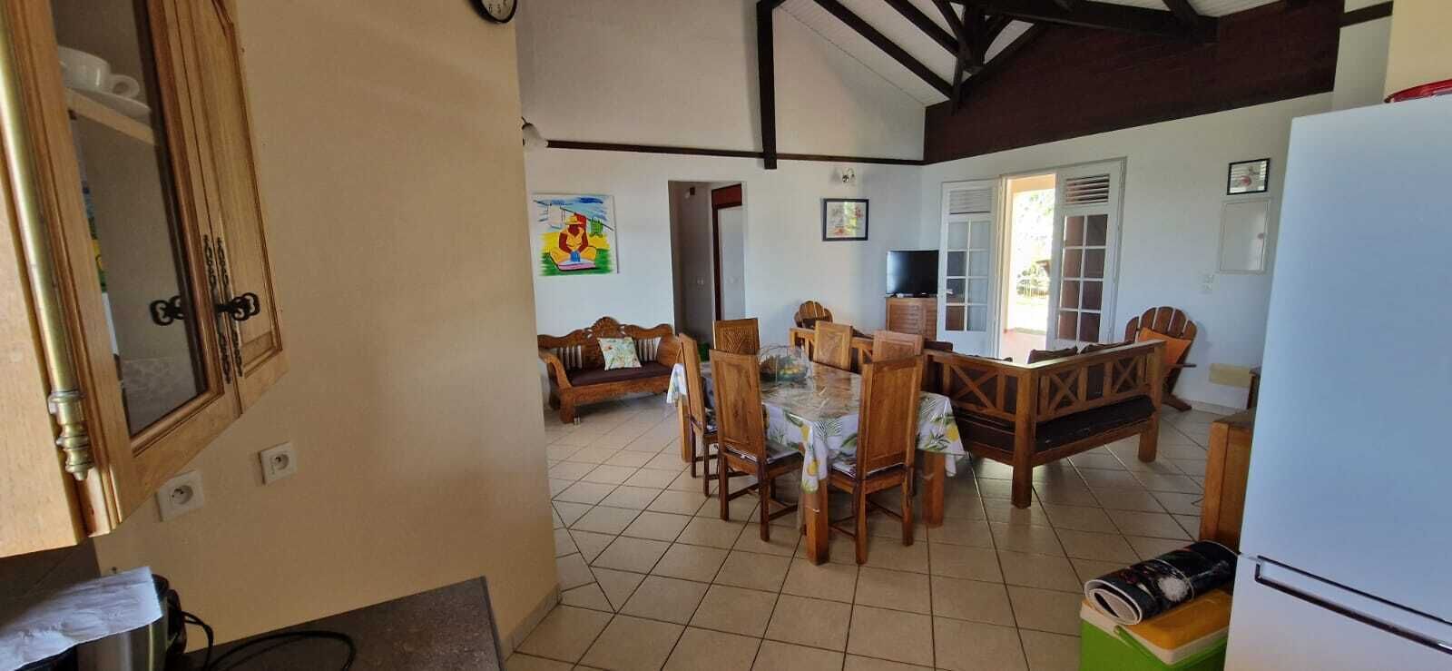 A dining area with a wooden table and chairs, a television, and a refrigerator.