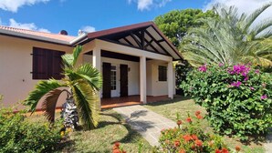 A two-story house with a covered porch, surrounded by lush greenery and flowering plants.