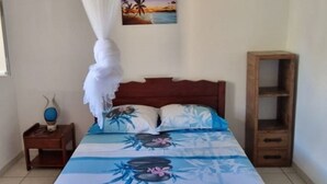 A bedroom with a bed, a nightstand, a wooden cabinet, a wall-mounted air conditioner, and a painting of a beach scene.