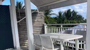 A covered outdoor area with a table and chairs, a wooden deck, and a view of palm trees.