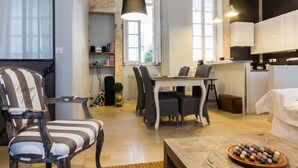 A modern living room with a striped armchair, a dining table with chairs, a coffee table with a bowl of marbles, and a kitchen area with cabinets and a hanging light fixture. - The Loisy - A very smart spot in the heart of Dijon for up to 4 people (Dijon)