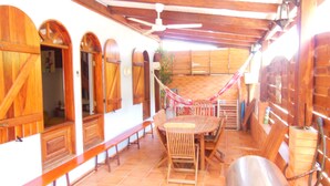 A covered patio area with wooden furniture, a hammock, and a ceiling fan.
