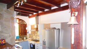 A kitchen with a stone wall, wooden beams, a gas stove, a refrigerator, and a bell.
