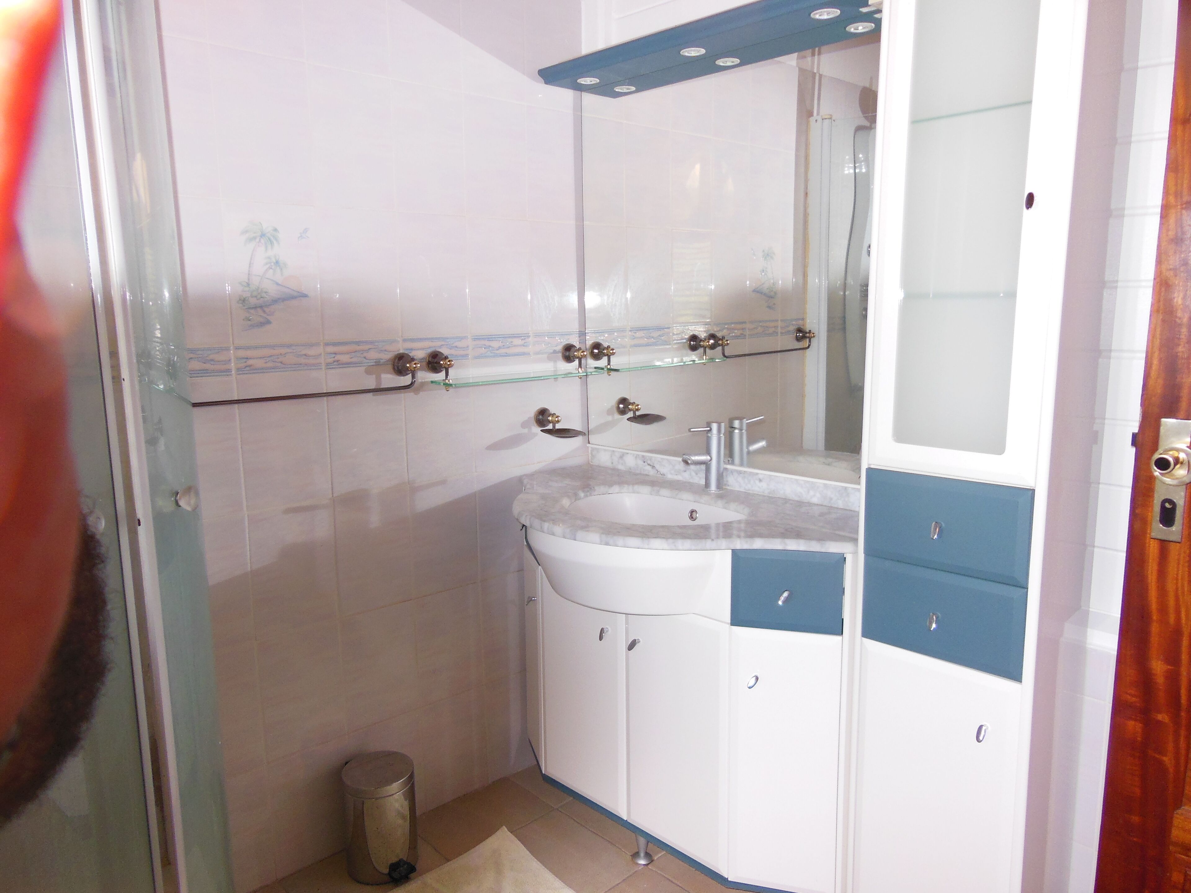 Un baño con un lavamanos blanco, armarios azules y una cabina de ducha de vidrio.