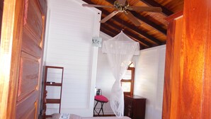 A bedroom with a bed, a ceiling fan, a wooden door, and a window with blinds.