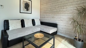 A modern living room with a sectional sofa, a glass coffee table, a wooden accent wall, and a potted plant. - Breton house in a typical seaside village - Sainte-Barbe (Plouharnel)