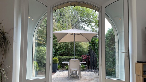 A glass door leading to an outdoor patio with a table and umbrella. - Breton house in a typical seaside village - Sainte-Barbe (Plouharnel)