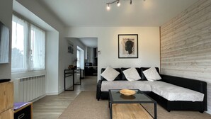 A modern living room with a black sofa, a glass coffee table, and a kitchen in the background. - Breton house in a typical seaside village - Sainte-Barbe (Plouharnel)