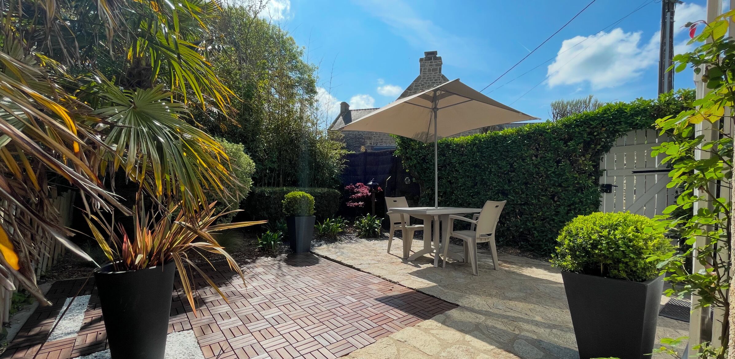 A patio with a table and chairs, surrounded by potted plants and a large umbrella.