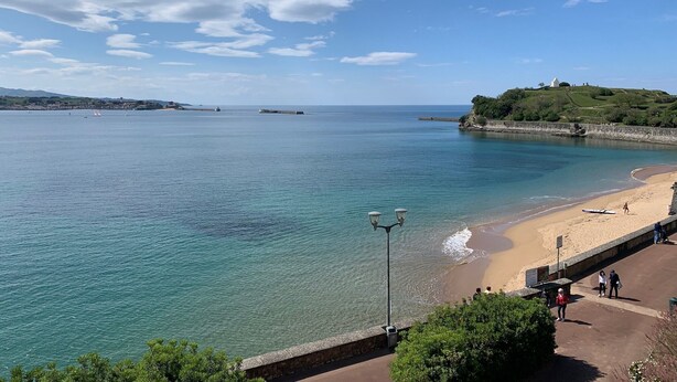 A coastal view with a sandy beach, calm sea, and a hill with greenery and a structure on top. - Breathtaking sea view 1st ocean line - Contemporary decor (Saint-Jean-De-Luz)