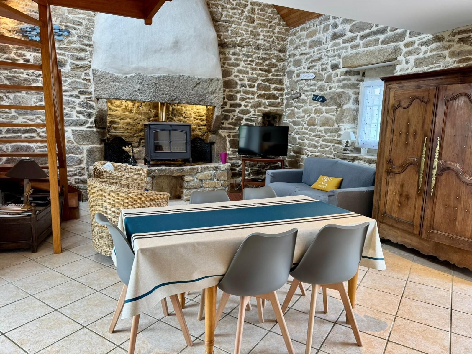 A cozy stone-walled room with a fireplace, a television, a sofa, and a dining table with chairs.