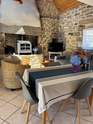 A cozy room with a stone wall, a fireplace, a television, and a dining area with a table set for two. - Vacation home between sea and countryside (Plozévet)