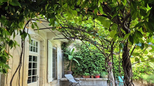 A covered porch with a chair, a potted plant, and a hose. - TOWNHOUSE WITH SWIMMINGPOOL - Country living in the city (Nîmes)