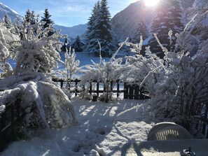 Paesaggio innevato con una recinzione in legno, alberi carichi di neve e una montagna sullo sfondo.