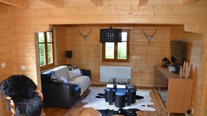 Interior de cabana de madeira com sofá, mesa de jantar com banquinhos, poltrona de pele e tapete de couro de vaca.