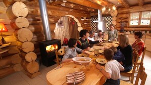 A rustic wooden interior with a central wood-burning stove, a dining table surrounded by chairs, and a checkered wall pattern. - Sublime chalet rondins de 140 m² en lisière de forêt et ruisseau, La Bresse, wifi (La Bresse)