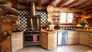 A rustic kitchen with a central stove, wooden cabinets, and a checkered backsplash. - Sublime chalet rondins de 140 m² en lisière de forêt et ruisseau, La Bresse, wifi (La Bresse)