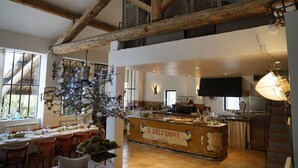 A spacious dining area with a high ceiling and exposed wooden beams, a central bar area with a sign reading "U DIEIDONE," and a view of the kitchen in the background. - Farmhouse in Provence, farmhouse, private in a 7 hectares park, heated pool (L'isle-Sur-La-Sorgue)