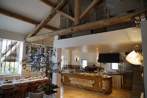 A spacious dining area with a high ceiling and exposed wooden beams, a central bar area with a sign reading "U DIEIDONE," and a view of the kitchen in the background. - Farmhouse in Provence, farmhouse, private in a 7 hectares park, heated pool (L'isle-Sur-La-Sorgue)