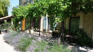 A building with a stone facade, a balcony with a table and chairs, and a garden with lavender plants. - Farmhouse in Provence, farmhouse, private in a 7 hectares park, heated pool (L'isle-Sur-La-Sorgue)