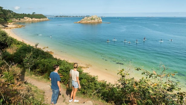 A coastal scene with a clear view of the sea, a sandy beach, and a small rocky island.