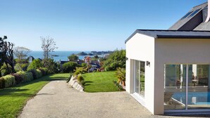 A modern house with a clear view of the sea, a gravel path, and a well-maintained garden.
