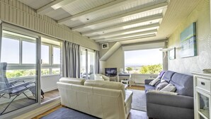 A spacious living area with a large sofa, a smaller grey sofa, a TV, and a dining area with a table and chairs.