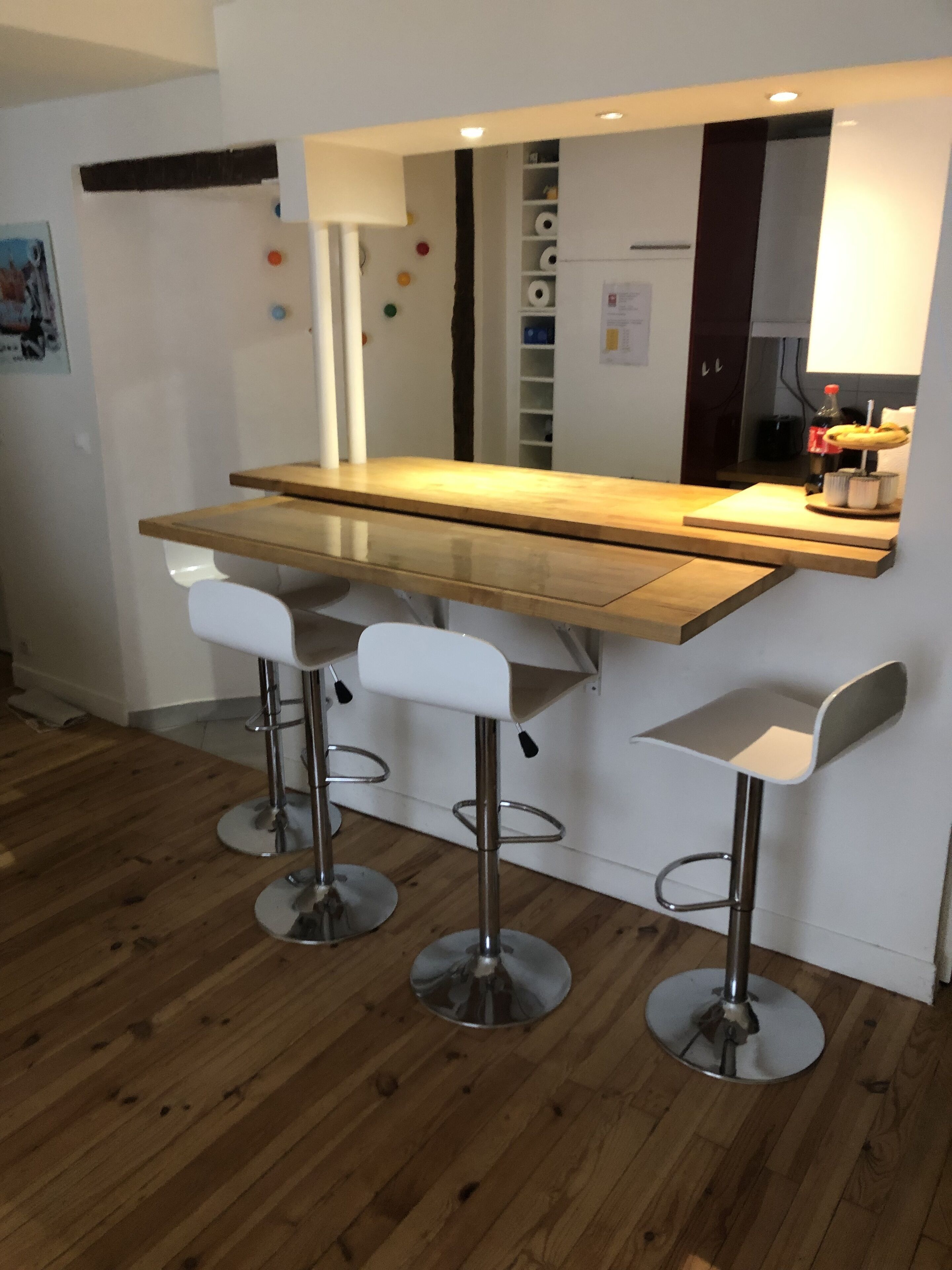A modern kitchen with a wooden countertop, three bar stools, and a built-in refrigerator.