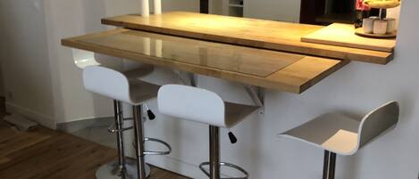 A modern kitchen with a wooden countertop, three bar stools, and a built-in refrigerator.