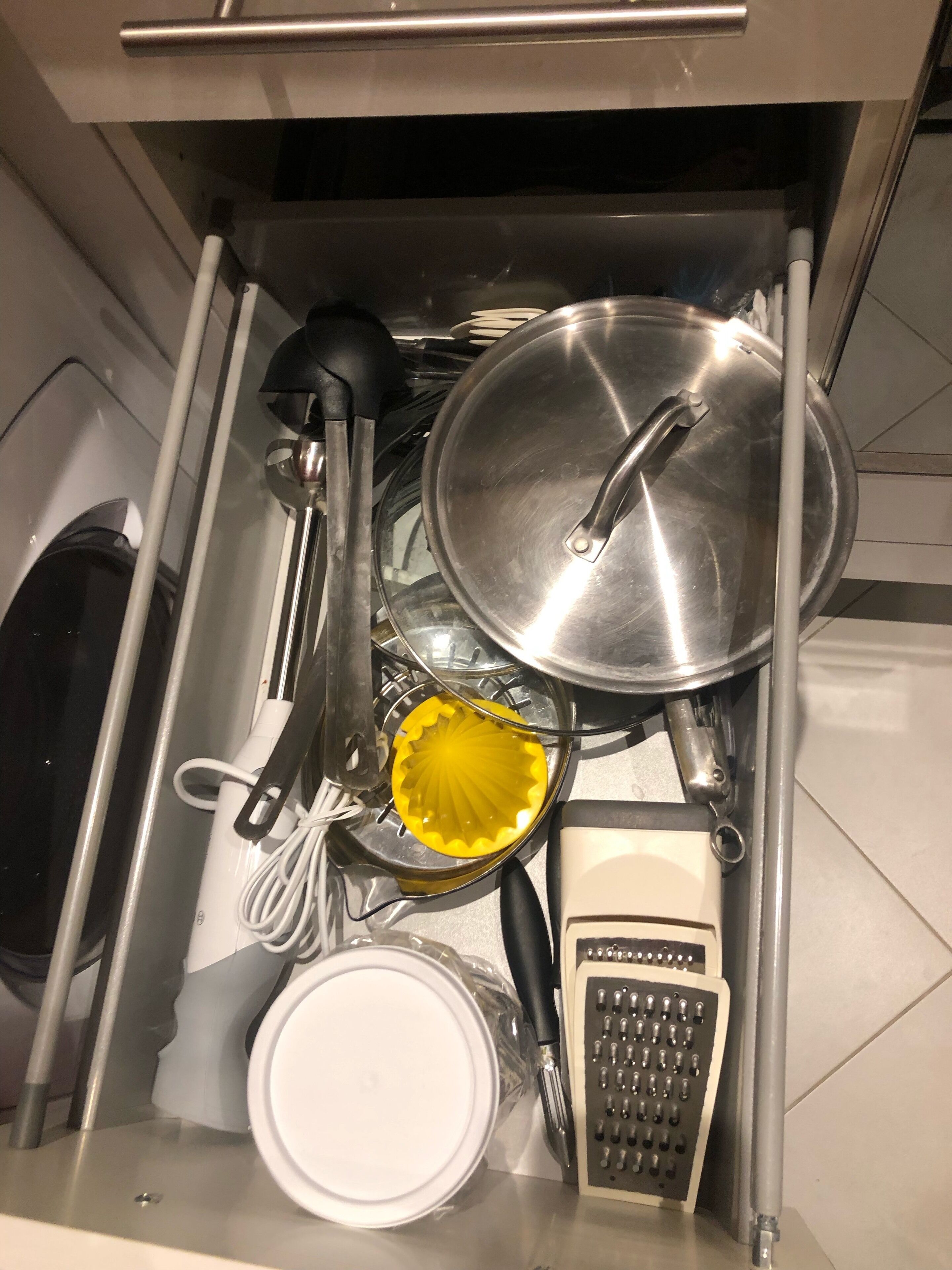 Een keukulaag met een rasp, een gele citruspers, een pan met deksel en een witte bak.
