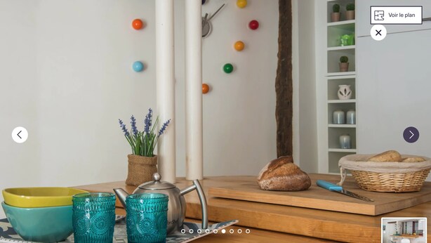 A kitchen with a wooden countertop, a teapot, a bread loaf, and a basket with bread.