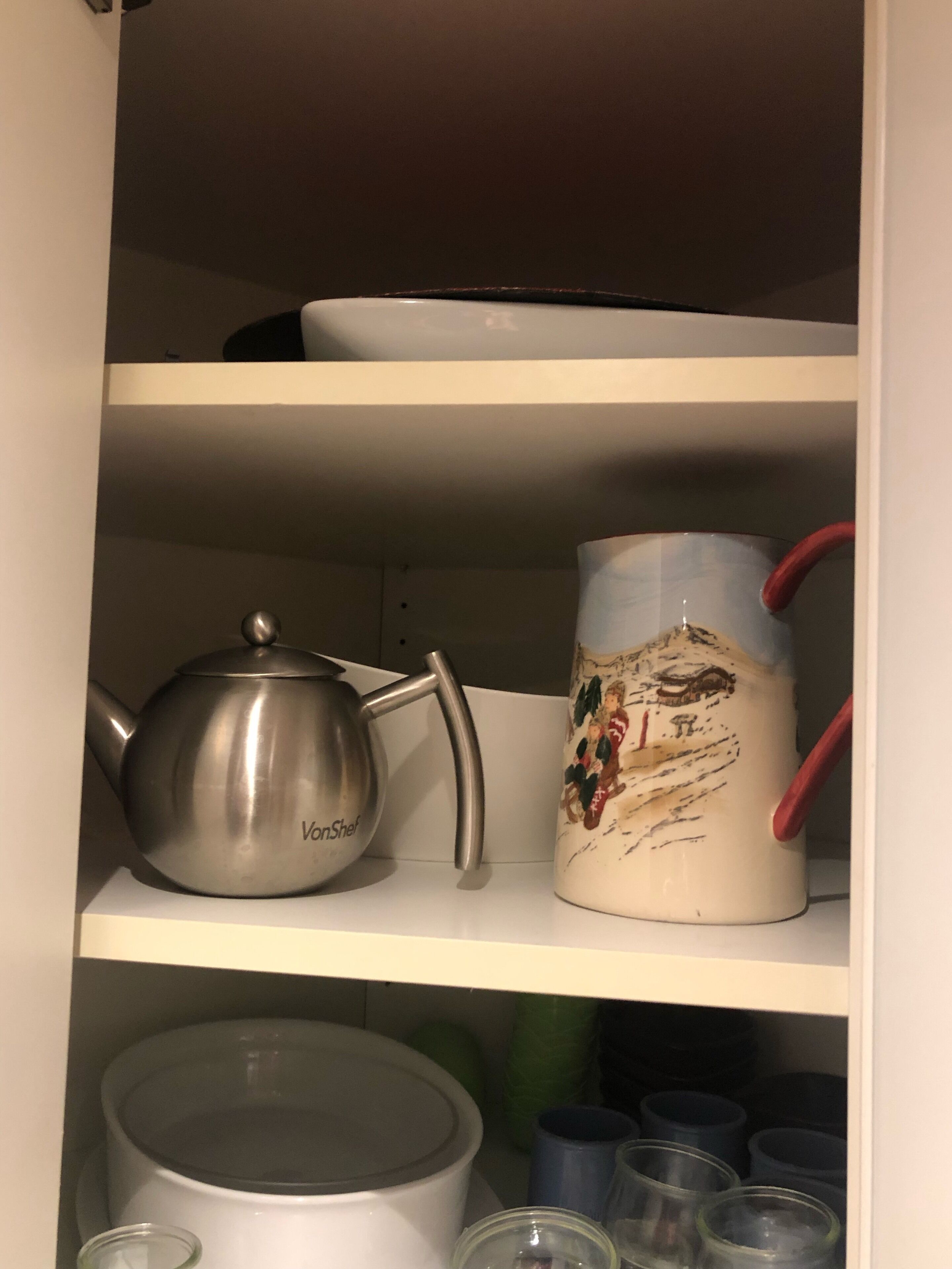 Ein Küchenregal mit einem Edelstahl-Teekessel und einer Keramiktasse mit weihnachtlicher Szene.