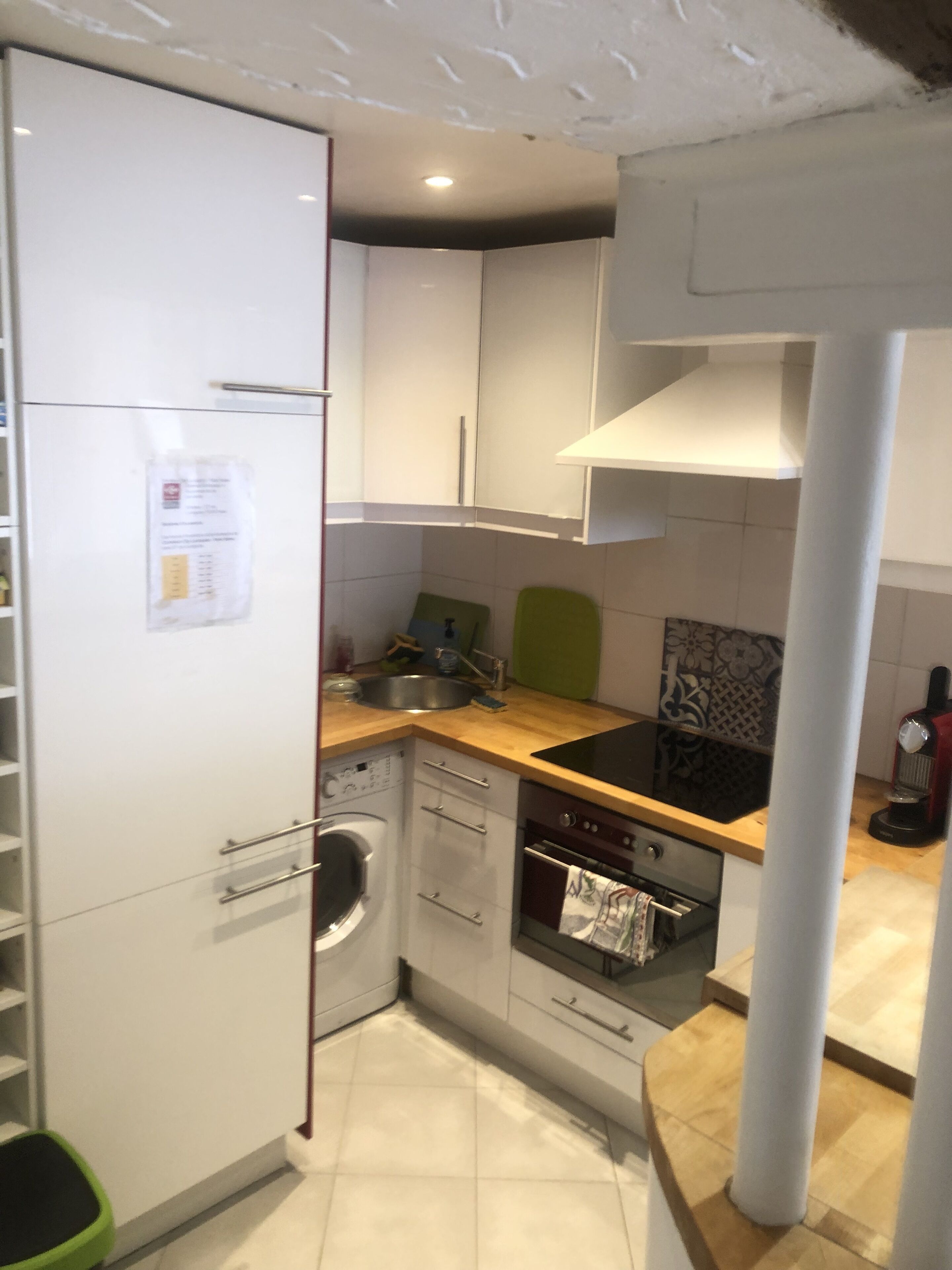 Une cuisine compacte avec des meubles blancs, un lave-linge encastré, une cuisinière et un évier.