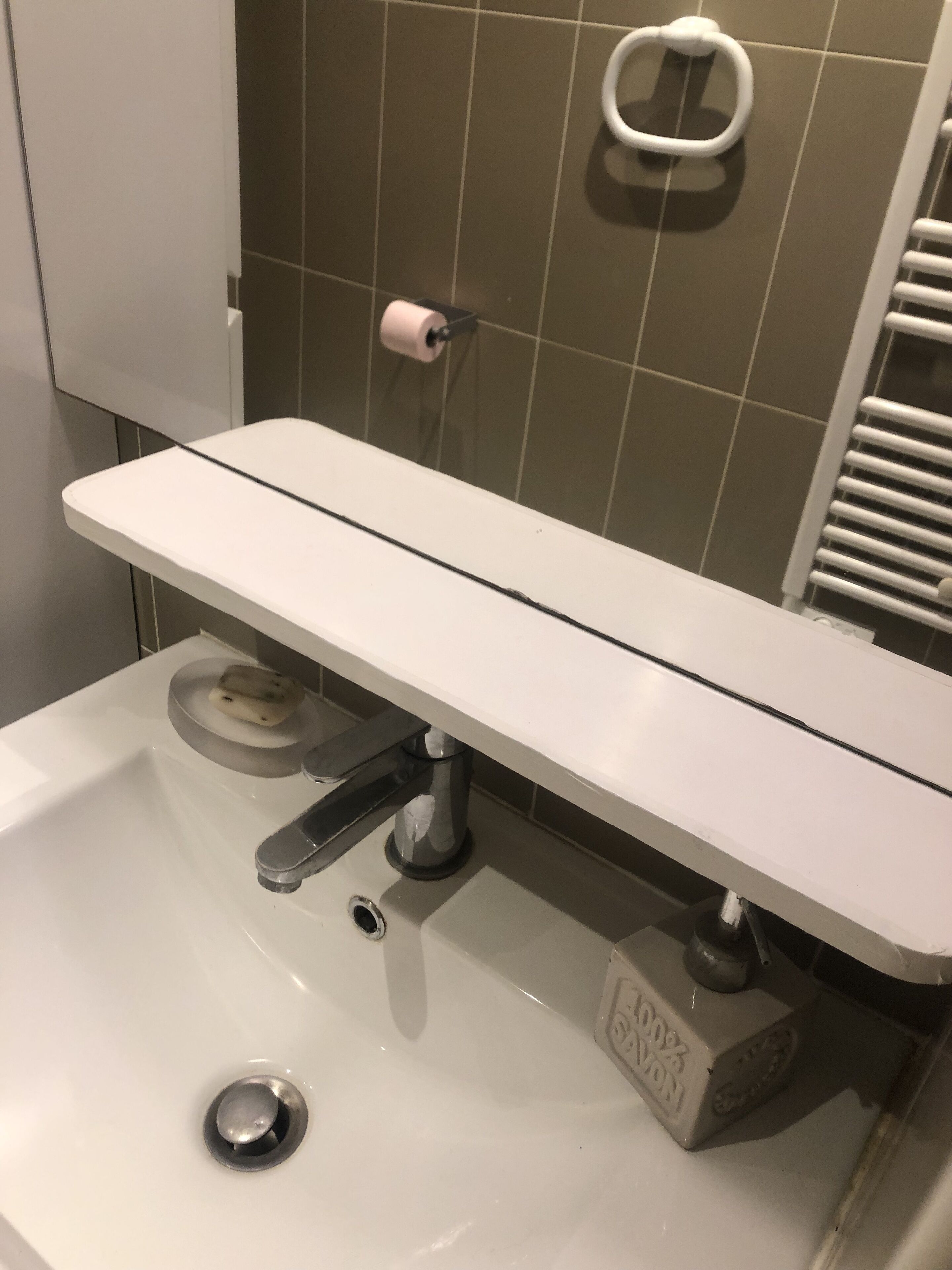 A bathroom sink with a white countertop, a soap dish, and a paper towel holder.