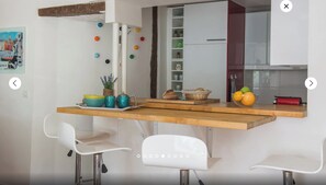 Une cuisine moderne avec un plan de travail en bois, des chaises blanches et divers ustensiles de cuisine.