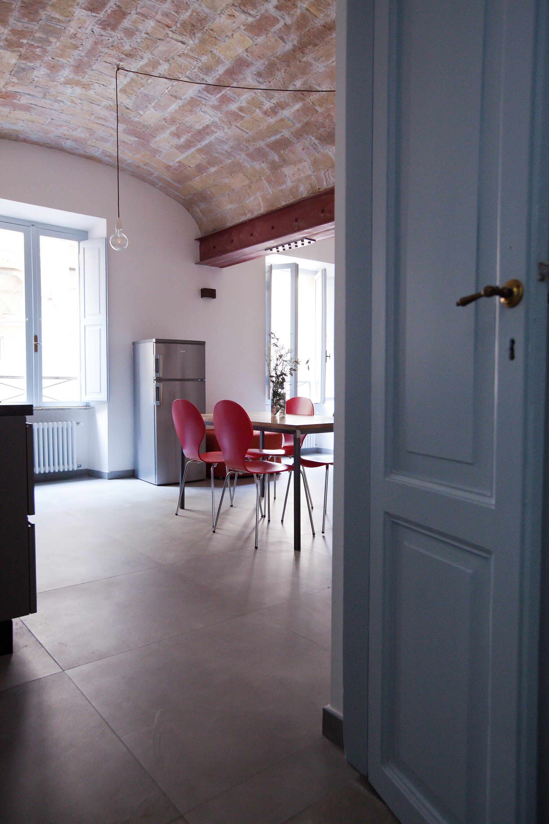 A kitchen with a refrigerator, a dining table with chairs, and a door leading to another room.