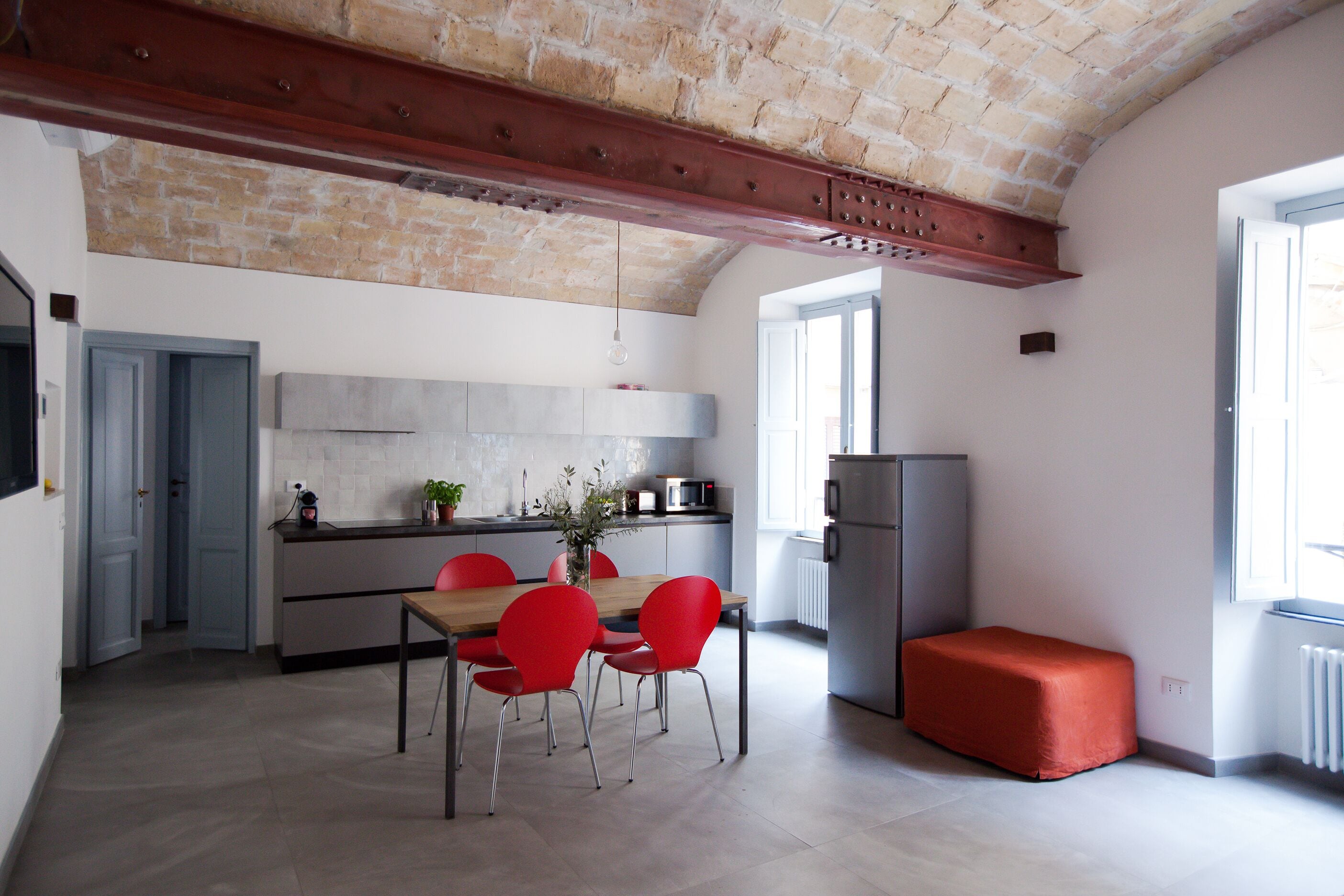 A modern kitchen with a dining area, featuring a brick ceiling, a built-in oven, and a red bench.