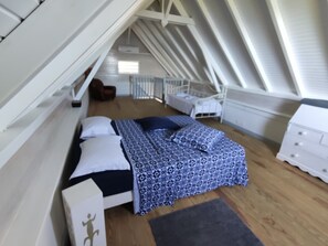 A bedroom with a sloped ceiling, a bed with patterned bedding, a chair, a dresser, and a small table. - Small furnished house with pool Le Robert Martinique (LE ROBERT)