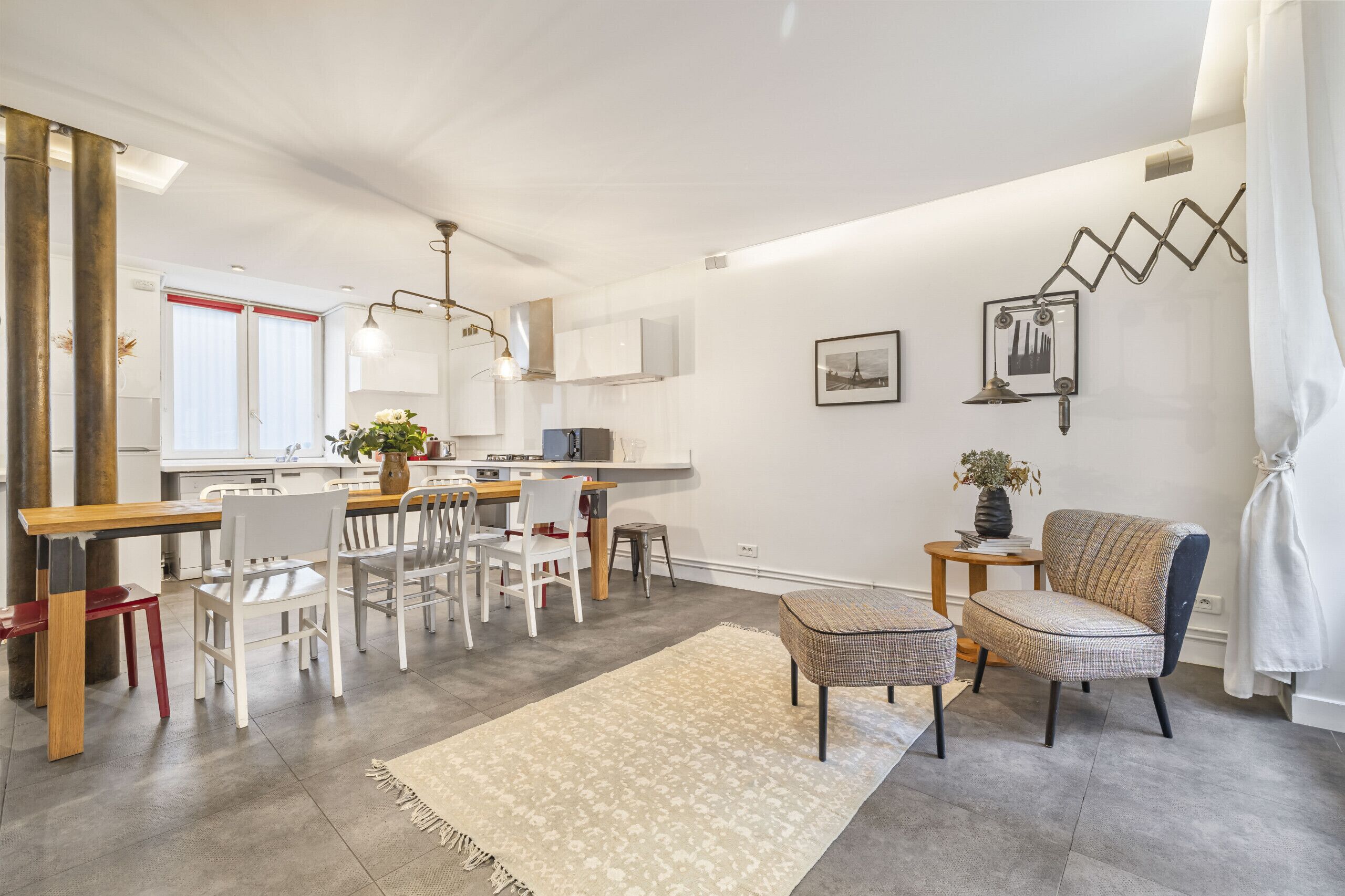 Cozinha moderna com armários brancos, espaço de refeições com mesa e cadeiras de madeira, e sala de estar com sofá e tapete.