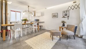 A modern kitchen with white cabinets, a dining area with a wooden table and chairs, and a living area with a sofa and a rug. - Bahia, 2BR/1BA, 7 people (París)