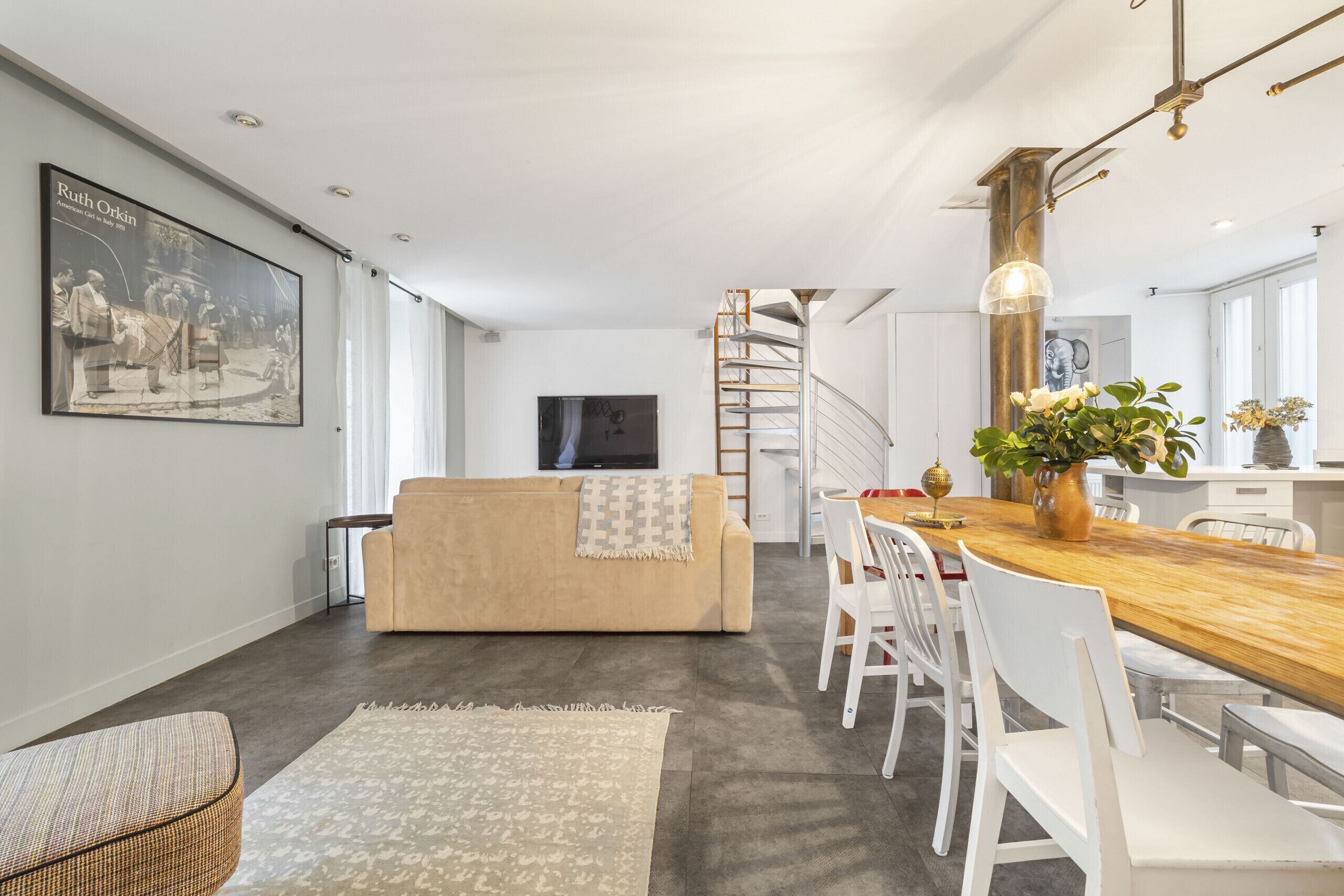 Ein modernes Wohnzimmer mit einer Couch, einem Esstisch mit Stühlen, einer Treppe und einem großen gerahmten Bild an der Wand.