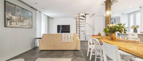 Una sala de estar moderna con un sofá, una mesa de comedor con sillas, una escalera y un cuadro grande en la pared.