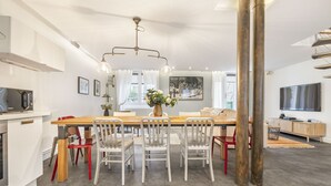 A modern kitchen with a dining area, white cabinetry, and a large wooden table. - Bahia, 2BR/1BA, 7 people (París)